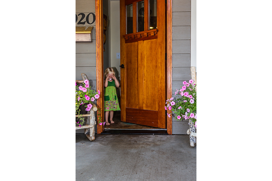 The young girl faces the viewer, standing in the doorway rubbing her eyes and sucking on a binkie.